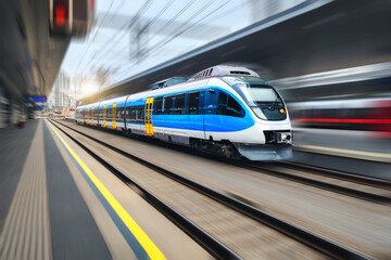 Wall Mural - High speed train in motion on the train station at sunset. Blue modern intercity passenger train with motion blur effect. Railway platform. Railroad in Europe. Commercial transportation. Concept