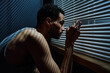 Side view view of young sleepless man looking through venetian blinds on window during sneak peek after someone outdoors