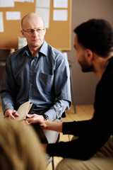 Wall Mural - Confident mature counselor looking at one of patients with post traumatic disorder while listening to him during session