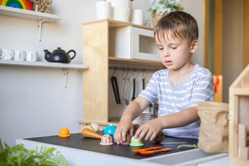 Wall Mural - Cute male kid preparing toy food boiling vegetables on cooker at childish room kitchen