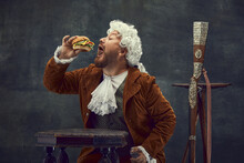 Fast Food. Vintage Portrait Of Young Man In Brown Vintage Suit And White Wig Like Medieval Royal Hunter Isolated On Dark Background.