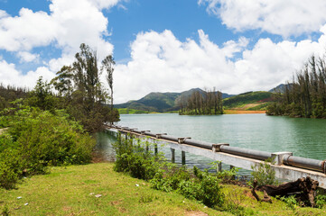 Wall Mural - Towering mountains, river with visible small island, blue and white sky, reflection visible in water, nature's gift of greenery everywhere is the way one can explain the beauty of Ooty.