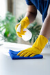 © kamiphotos - Person cleaning the room, cleaning staff is using cloth and spraying disinfectant to wipe the tables in the company office room. Cleaning staff. Maintaining cleanliness in the organization.