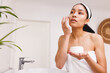 © Wavebreak Media - Happy biracial woman looking at mirror and applying cream on face in bathroom