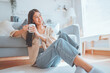 © oatawa - Happy young asian woman drinking coffee relaxing on the rug beside to the sofa at home. Smiling female enjoying resting sitting on couch in modern living room.