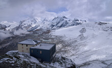 Hornli Hut Located At The Foot Of The Hornli Ridge, That Separates East And North Faces Of Mount Matterhorn. Panoramic View On Surrounding Mountains. Hornli Hut Above The Clouds In A Snowy Autumn Day.