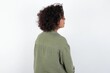 © Roquillo - The back side view of a young beautiful woman with curly short hair wearing green overshirt over white wall. Studio Shoot.
