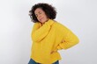 © Roquillo - young beautiful woman with curly short hair wearing yellow sweater over white background got back pain
