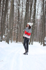 Wall Mural - A young woman in a sweater and a white hat in the forest. Full length portrait. Snowing. Winter atmosphere. Walk in the forest.