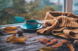 Cup of coffee on a wooden autumn background. Tea and autumn leaves near the window. Coffe on the background of a window with rain.