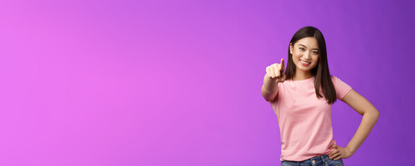 We need you our team. Friendly good-looking outgoing asian woman brunette pointing camera, indicate index finger, smiling motivated, picking person, making decision, stand purple background