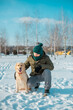 © trofalena - Owner man in snow clothes resting with his dog golden retriever outdoors in winter park, during cold snow day. Obedient practicing sit command.