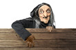 Old witch in a cloak standing behind a wooden board