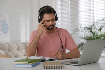 Wall Mural - Confused young man watching webinar at table in room