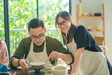 Focus couple potter working on potters wheel making ceramic pot from clay in pottery workshop. Couple in love working together in potter studio workshop.