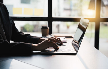 Close-up businessperson typing and searching data internet on laptop and hands holding pen at office desk, Online learning concept.