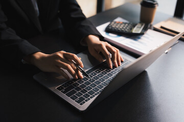 Close-up businessperson typing and searching data internet on laptop, graph diagram,  and calculator on office table, Online learning concept.