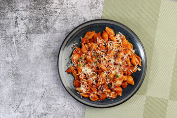 Wall Mural - Red chicken pasta with herbs, tomatoes and cheese on a round plate on a dark gray background. Top view, flat lay