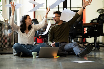 Wall Mural - Colleagues celebrating in the office. Businesswoman and businessman sitting on the floor. Colleagues working on the project.