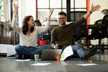 Wall Mural - Colleagues celebrating in the office. Businesswoman and businessman sitting on the floor. Colleagues working on the project.