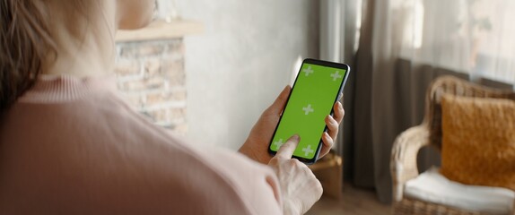 GREEN SCREEN CHROMA KEY Caucasian female using a phone inside her apartment. Vertical orientation. Scrolling and touch clicking center of the screen