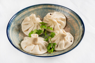 Sticker - Georgian traditional dumplings khinkali with meat filling and greens on a white dish.