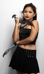 Wall Mural - Southeast Asian girl in a black top and skirt with two fantasy knives against a white wall