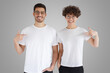 © Damir Khabirov - Daylight shot of smiling couple pointing at blank white t-shirts with finger, copy space for ads