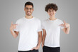 © Damir Khabirov - Smiling couple pointing at blank white t-shirts with index fingers, copy space for your advertising