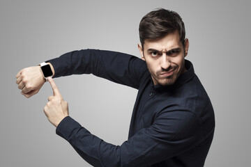 Wall Mural - Man pointing at watch with impatience as if asking to hurry up, isolated on gray background