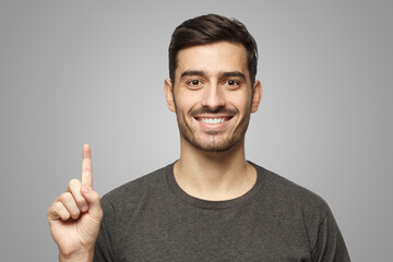 Wall Mural - Handsome young man pointing up with finger isolated on gray