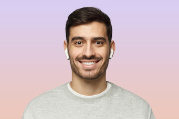 Wall Mural - Close-up portrait of young smiling handsome man with earphones isolated on pink