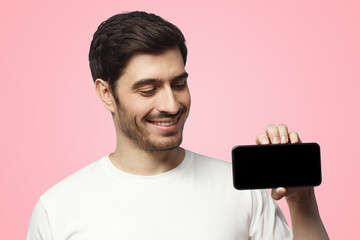 Wall Mural - Horizontal photo of young man showing blank screen smartphone in hand on pink backgroun