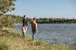 © Lyubov - Father and two sons walking along river bank. Family vacation in nature by water. Rear view of dad and children enjoying nature in countryside together.