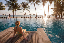 relaxation on beach, young woman enjoying beautiful sunset in luxury hotel near swimming pool