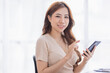 © David - Happy Excited Asian young entrepreneur business woman using phone and laptop sitting on a desk at home workplace,
