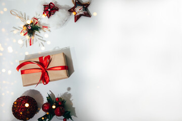 A gift wrapped in brown paper and tied red ribbon with toy star, a red ball and snowflake on a white background. Flat lay