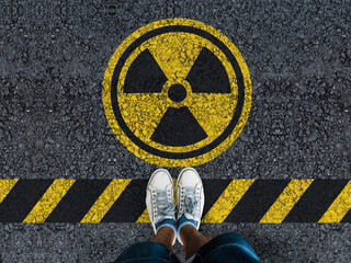 Wall Mural - man legs in sneakers standing on asphalt road and radioactive sign
