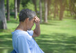 © Verin - senior man hand holding his head, older adult male look headache sitting under the shade of trees in the park after workout, risk of overexercising in elderly people