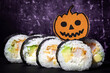 Sushi Halloween on dark background. Maki roll with festive pumpkin on top. Party food. Spooky, scary, fun California with avocado. Japanese sushi bar, restaurant holiday menu. Jack-o-lantern decor