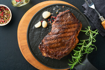 Steaks. Grilled New York Steak with spices rosemary and pepper on black marble board on gray background. Top view. Mock up.