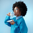 © Nicholas Felix/peopleimages.com - Afro hair, tea cup and black woman with fashion, style and trend clothes on blue background in studio with bold makeup cosmetics. Portrait, gossip and beauty model with wow or surprise face and drink