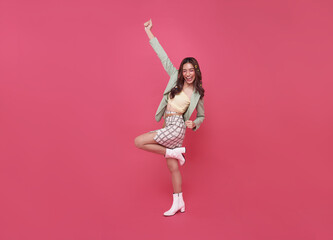 Happy Asian woman smiling and jumping while celebrating success isolated over pink background.