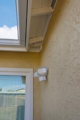 A white two-light motion sensor security light on a stucco wall of a home.