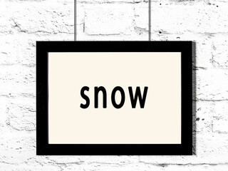 Black frame hanging on white brick wall with inscription snow