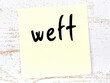 Yellow sticky note on wooden wall with handwritten word weft