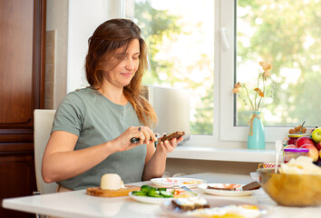 Healthy diet. A woman has breakfast at the table in the kitchen. A table with food and a nice woman buttering bread.