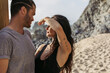 tattooed woman covering face with hand from sunshine near bearded boyfriend on beach in portugal.