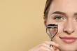 Woman with eyelash curler on beige background, closeup. Space for text