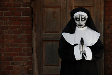 Wall Mural - Portrait of scary devilish nun with clasped hands near red brick wall, space for text. Halloween party look